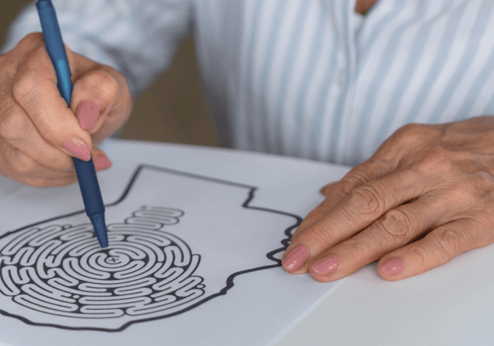 Sur l'image, nous pouvons voir une personne âgée en train de réaliser un parcours avec son crayon pour sortir du labyrinthe.