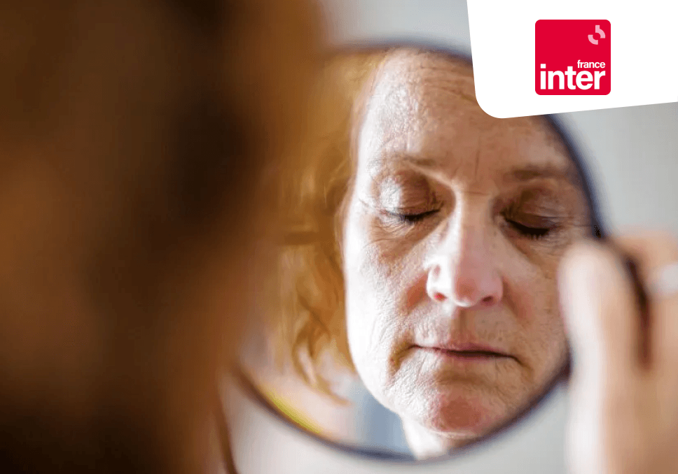 Sur l'image, nous pouvons voir une femme de 60 ans qui se regarde dans un miroir. En haut à droite, nous avons le logo de France inter, un carré rouge avec une typographie blanche.