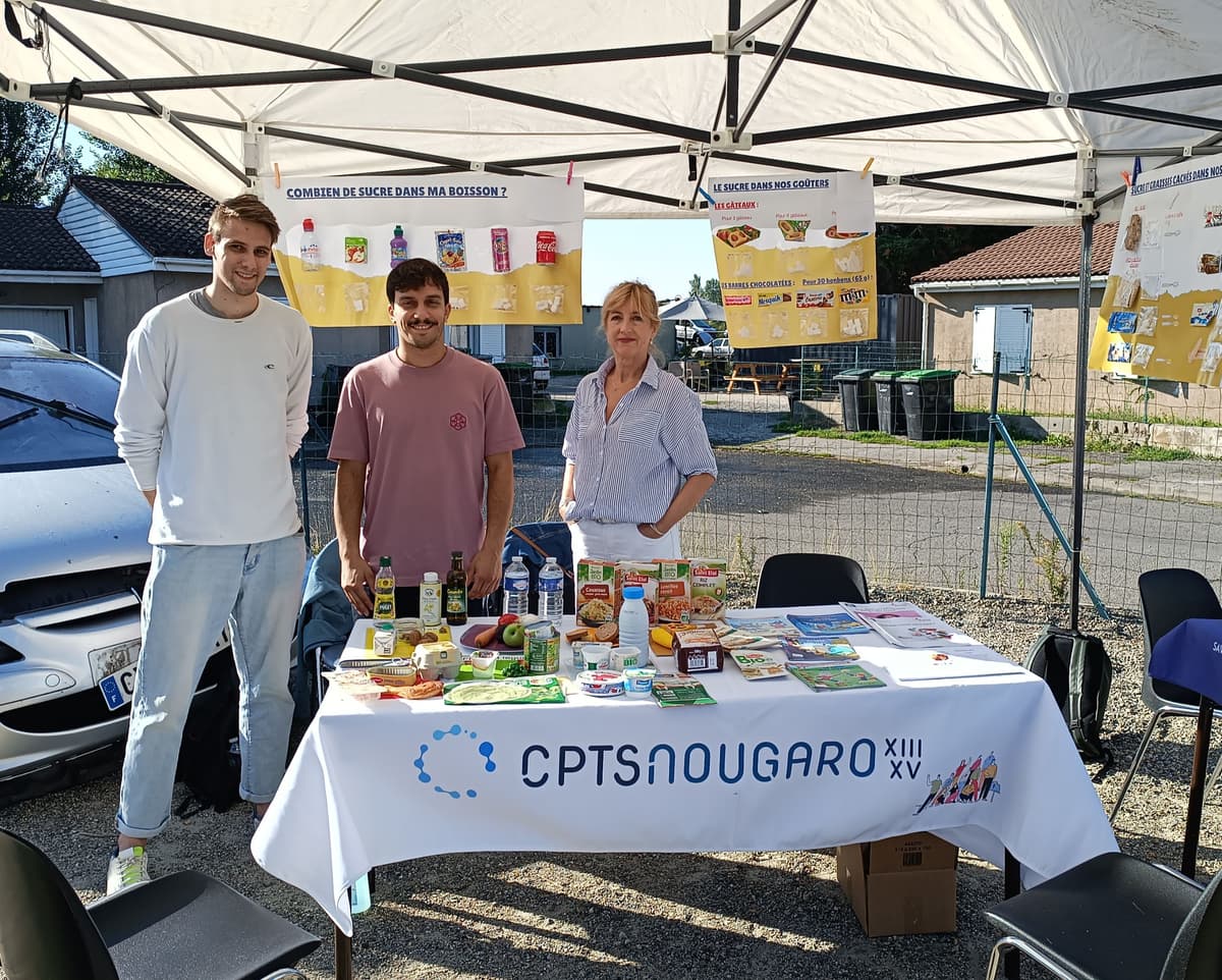 Sur l'image, nous pouvons voir trois professionnels de santé, derrière un stand en trian de regarder l'objectif.